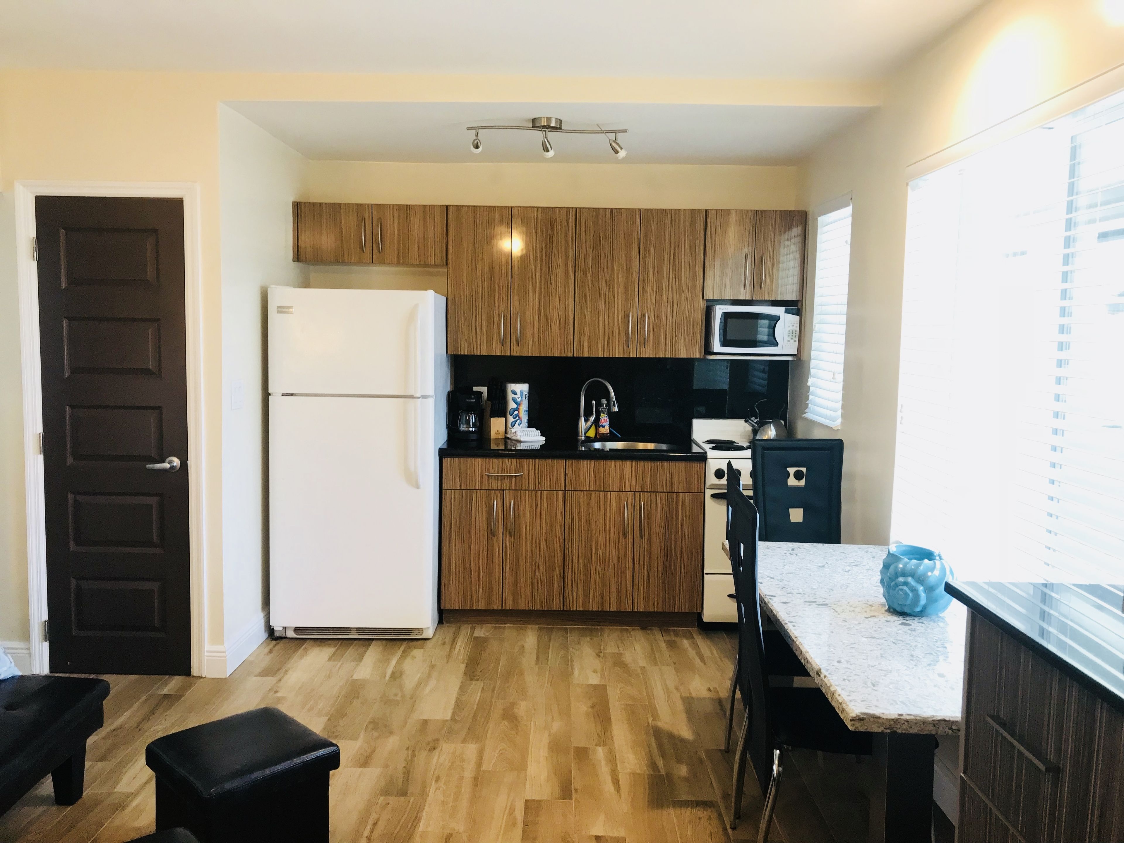 A compact kitchen with wooden cabinets, a white refrigerator, a microwave, and a stove. There is a small dining area with a table and chairs.