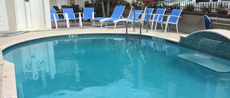 A swimming pool with blue lounge chairs and a white fence.