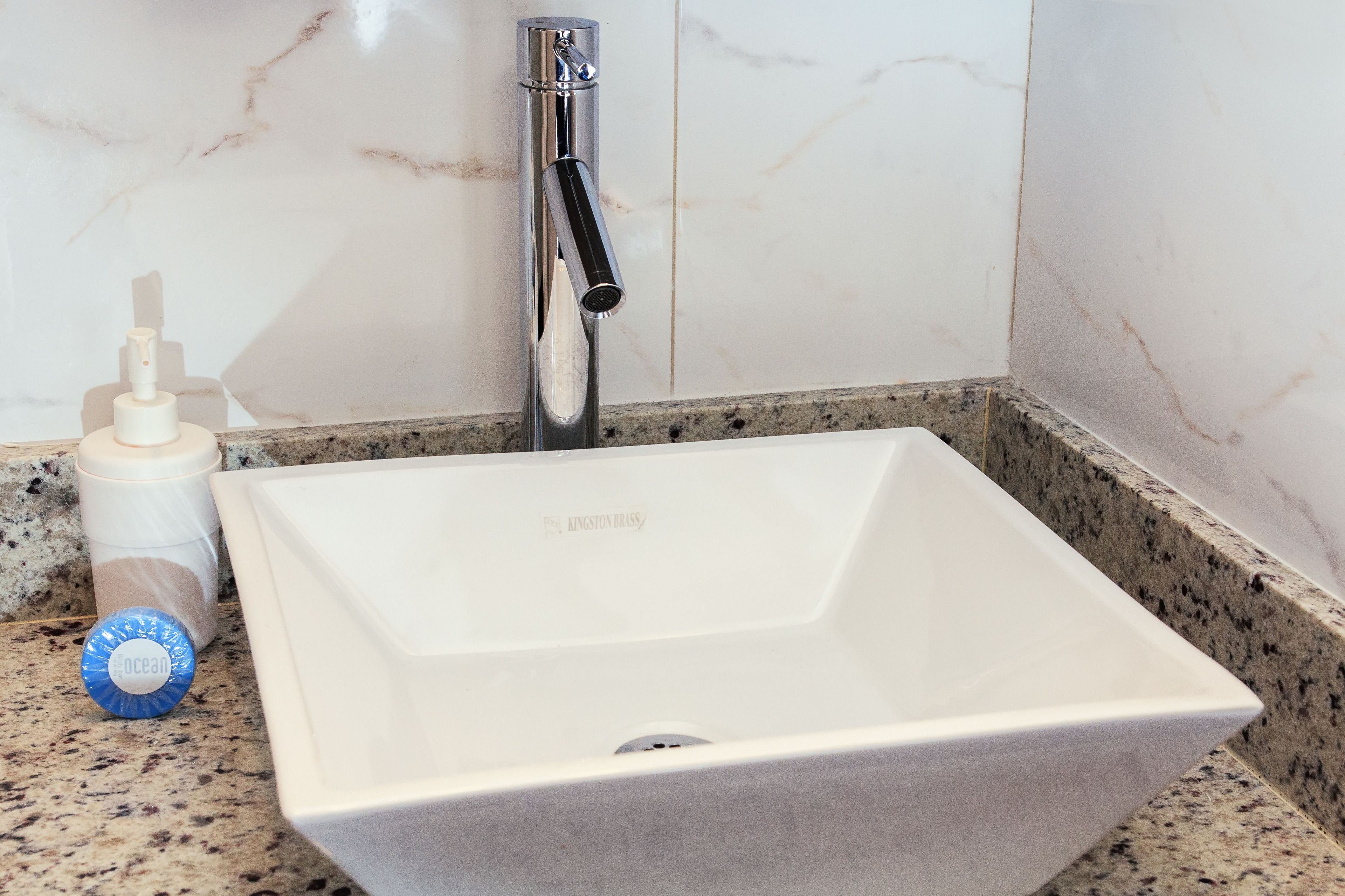 Un lavamanos con grifo cromado, una botella de jabón para manos y una pared de mármol.