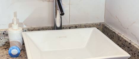 Un lavamanos con grifo cromado, una botella de jabón para manos y una pared de mármol.