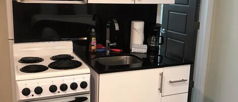 Una cocina compacta con armarios blancos, microondas, estufa y pileta.