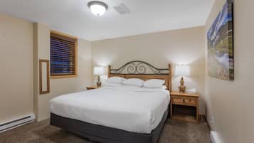 A bedroom with a large bed, two bedside tables with lamps, a window with blinds, and a painting on the wall.