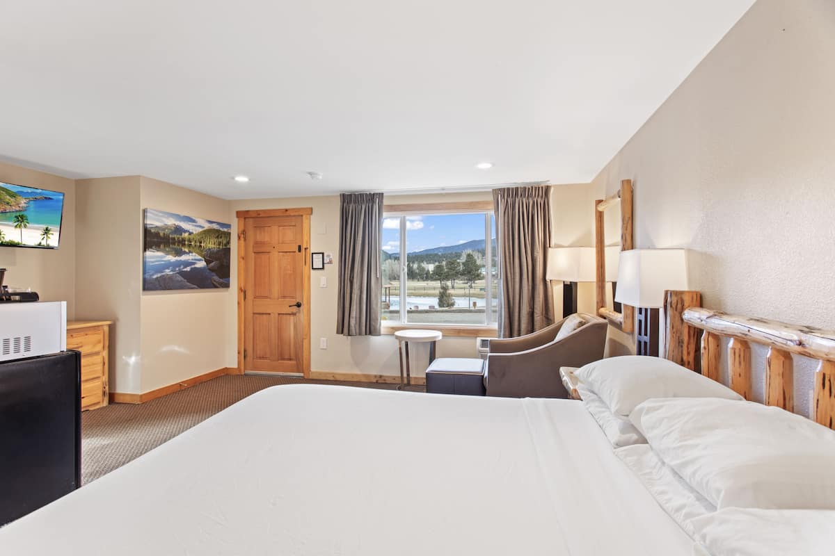A hotel room with a large bed, a desk, a chair, a small table, and a window with a view of the outdoors.