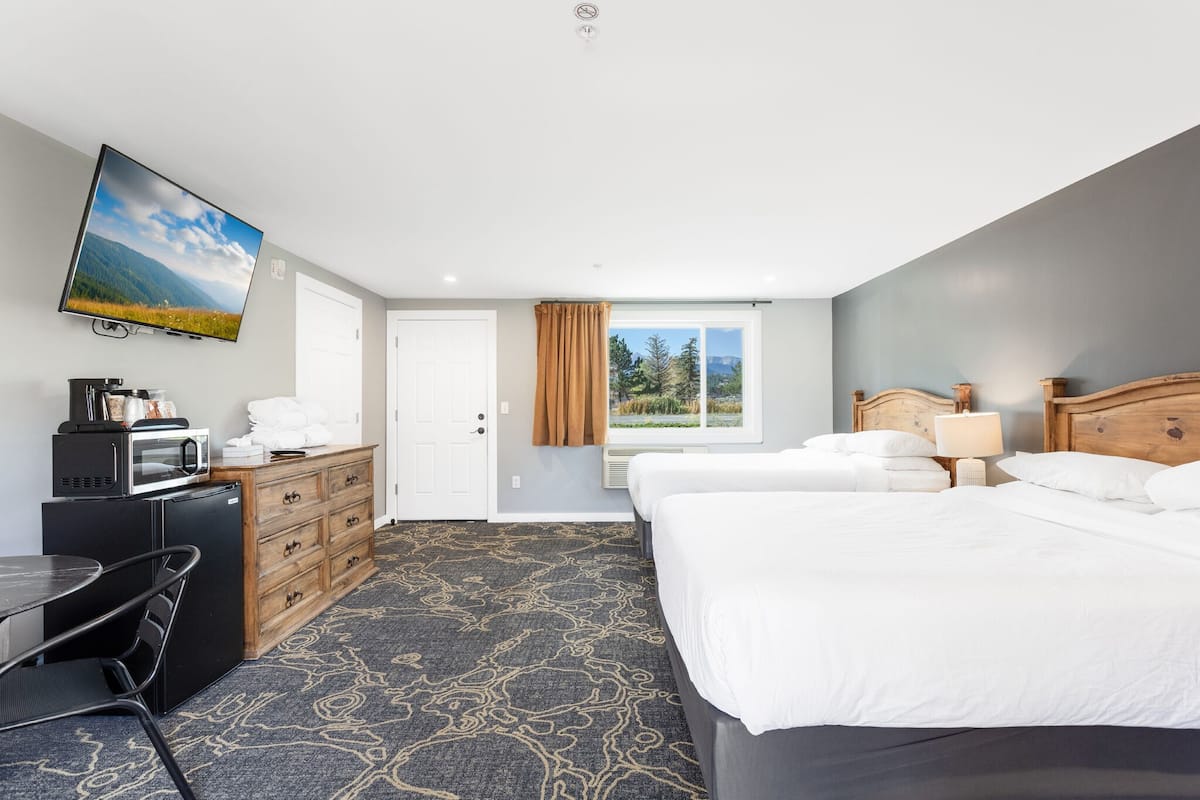A hotel room with a large bed, a desk with a chair, a television mounted on the wall, and a window with a view of trees.