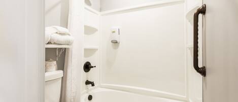 A white bathroom with a bathtub, a toilet, and a shelf with towels.
