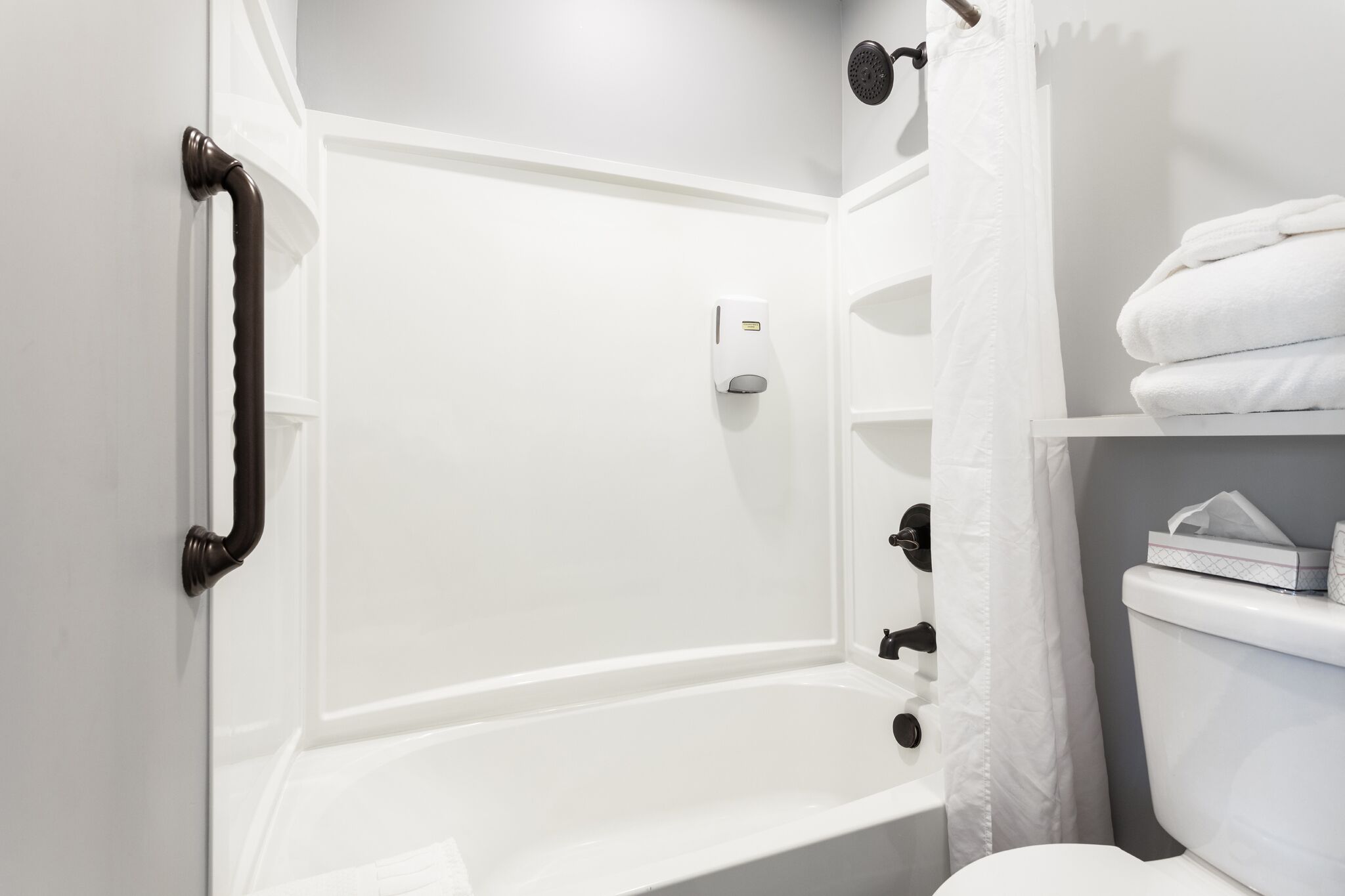 Une salle de bain blanche avec une baignoire, des toilettes et une étagère avec des serviettes.