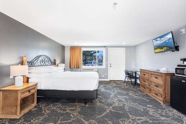 A hotel room with a bed, bedside table, desk, and a TV on the wall. - Discovery Lodge (Estes Park)