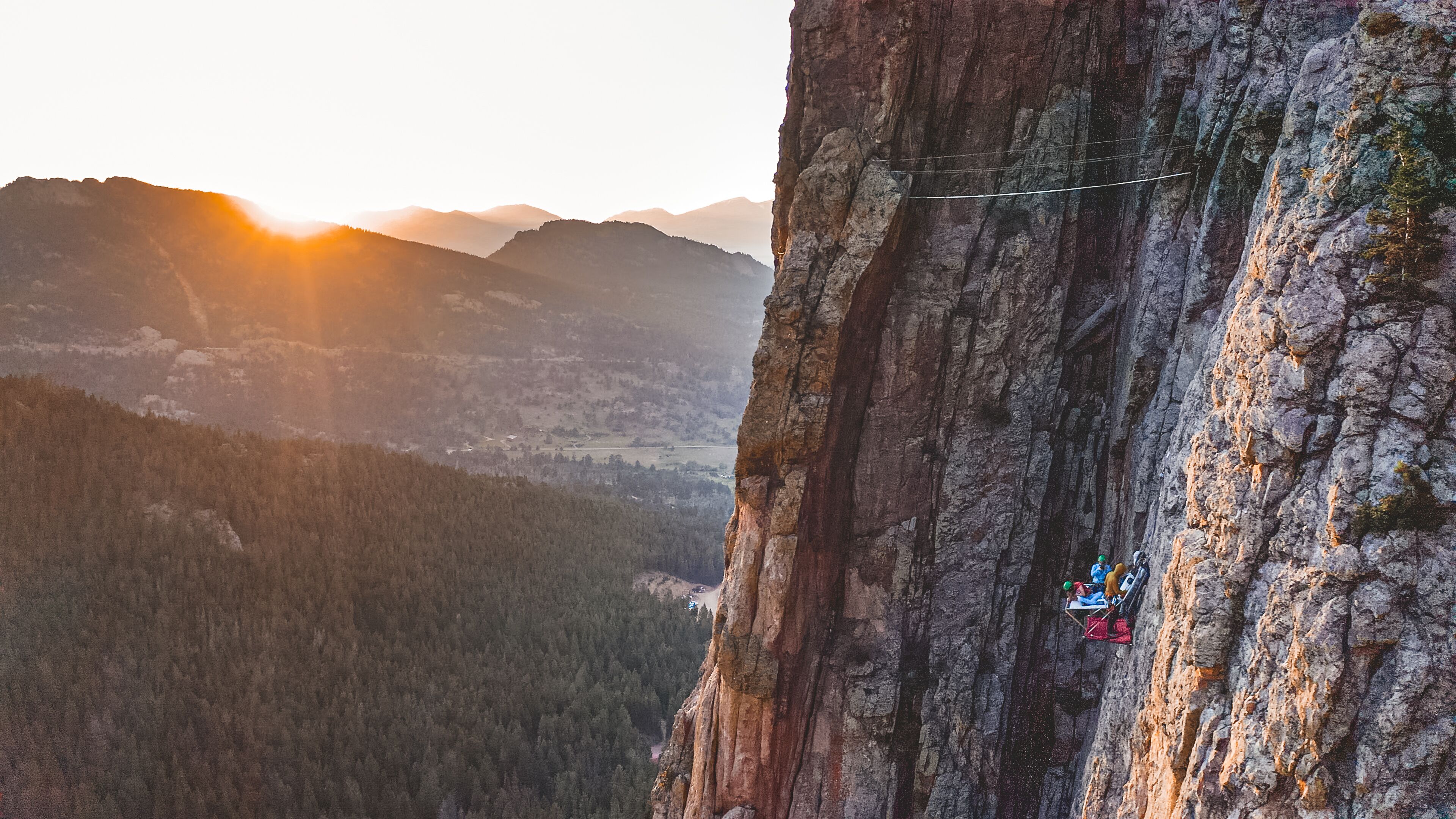 Paisaje montañoso con un risco rocoso y una persona descendiendo en rappel.
