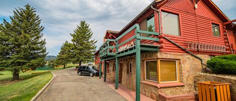 A red log cabin with a stone foundation, a covered porch, and a small attached structure.
