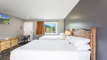 Habitación de hotel con una cama grande, un escritorio, una silla, un ventanal con vistas a las montañas y un televisor en la pared.