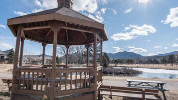 Un quiosco de madera con banca y mesa de picnic, con vistas a un lago y montañas.