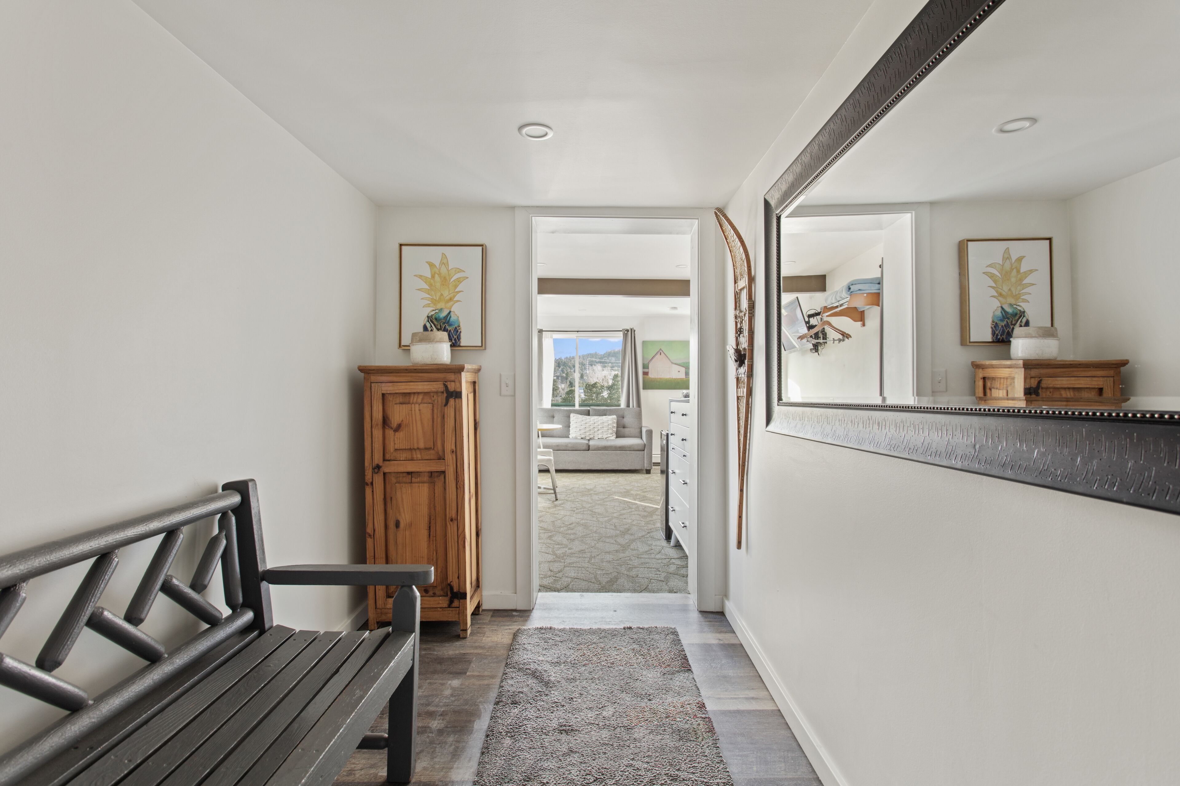 A hallway with a bench, a wooden cabinet, a mirror, and a view into a living area.
