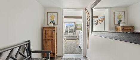 A hallway with a bench, a wooden cabinet, a mirror, and a view into a living area.