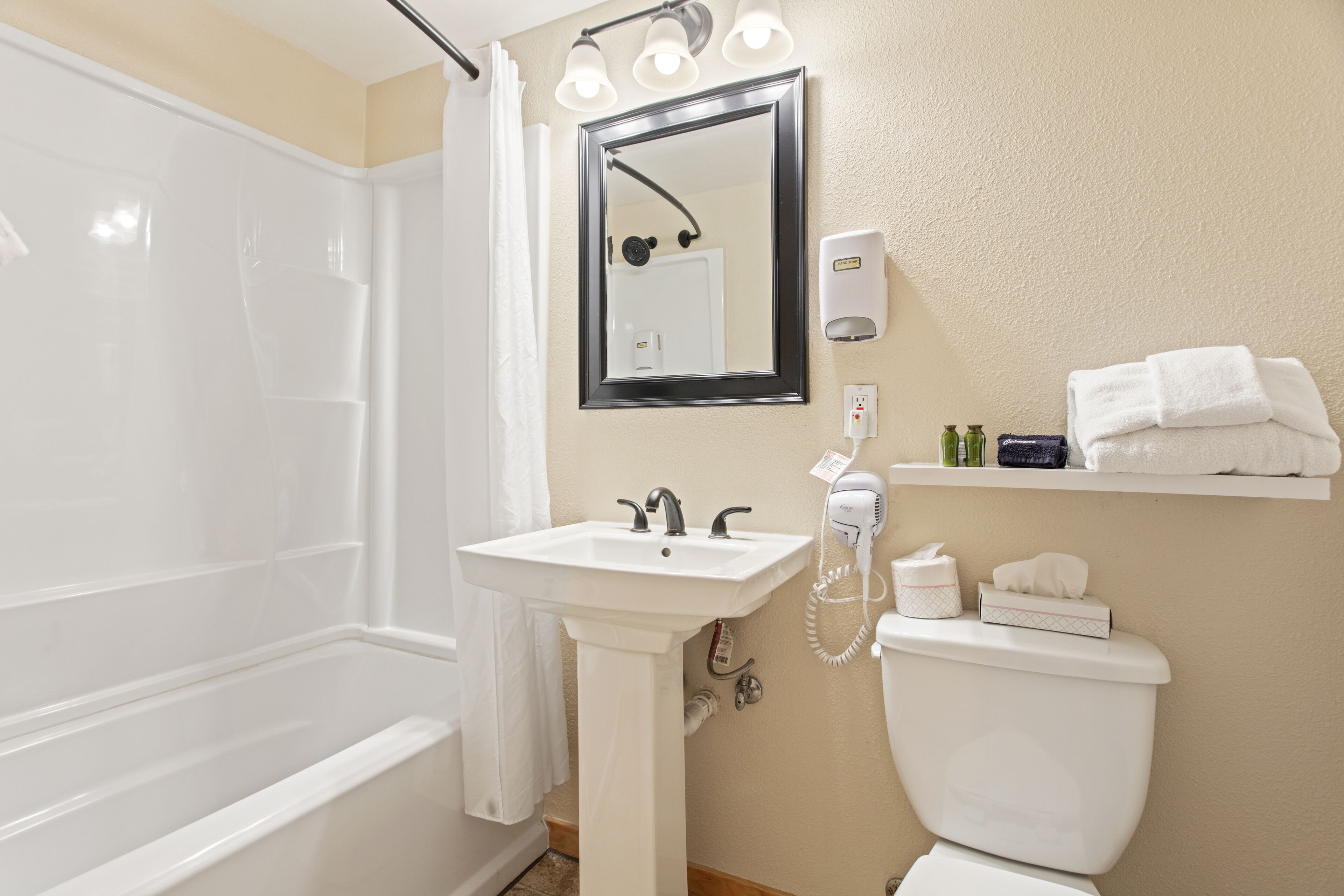 A bathroom with a bathtub, sink, mirror, and toilet. There are towels and toiletries on the wall.