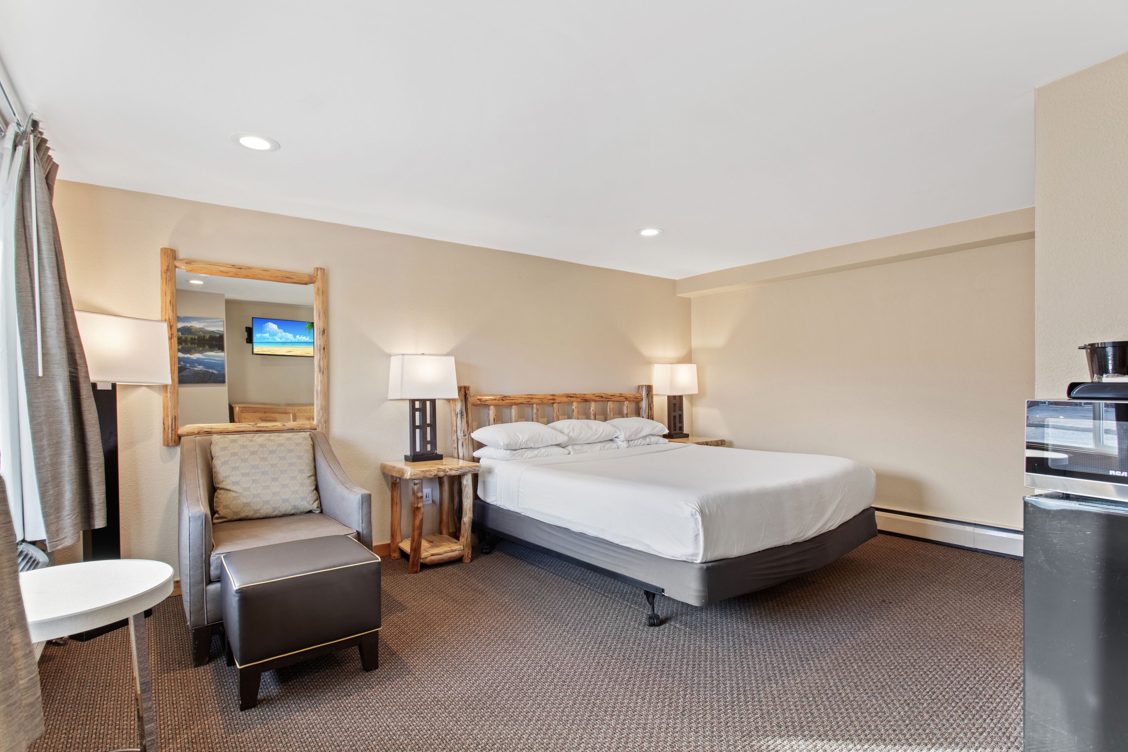 A hotel room with a bed, a chair, a desk, a mirror, and a TV.