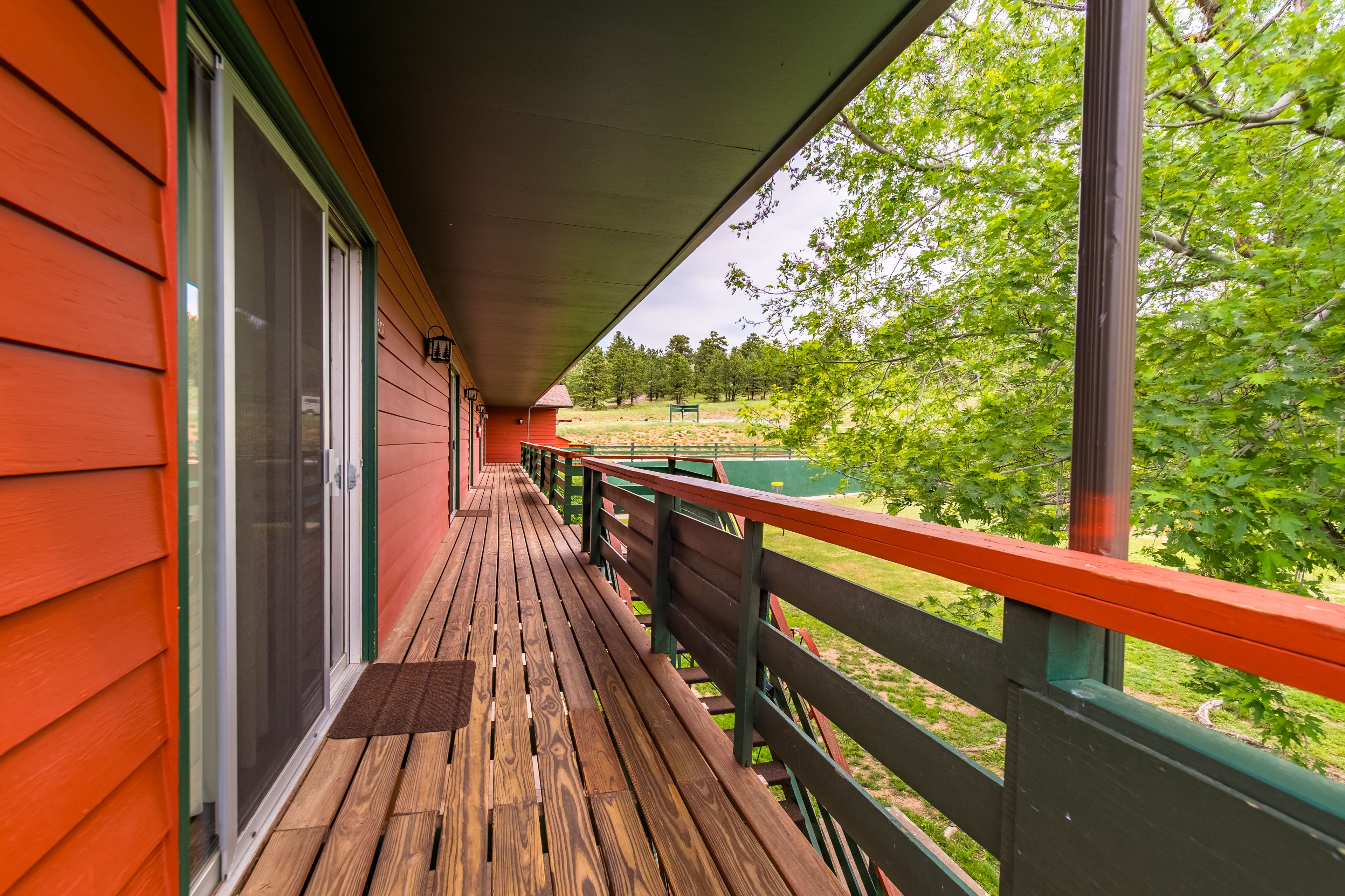 Una terraza de madera con un ventanal de vidrio que da a un espacio cubierto, con vista a un paisaje verde.