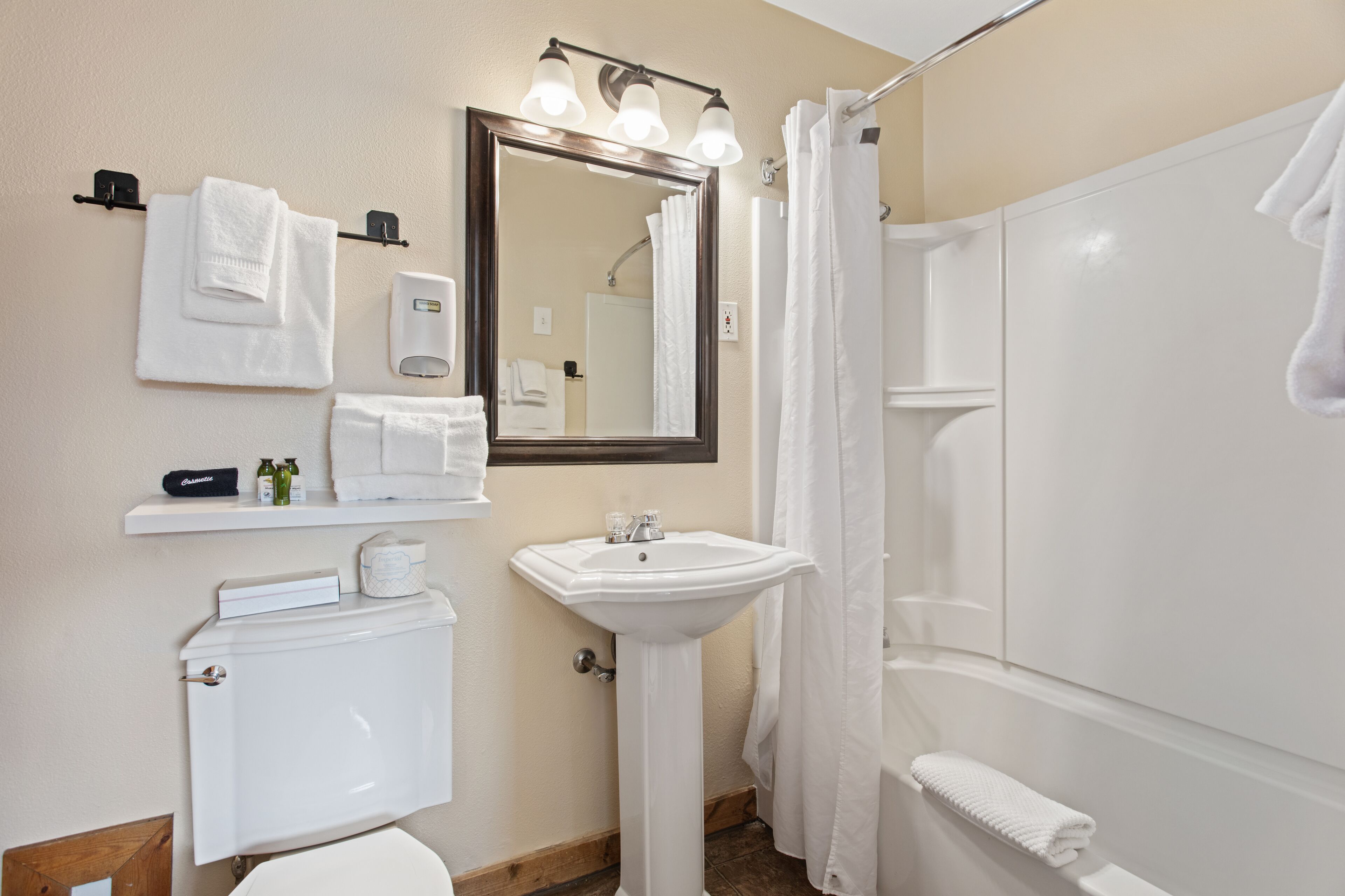 A bathroom with a toilet, sink, mirror, and shower. There are towels and toiletries on the wall.