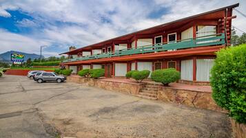 A two-story motel with a red and green exterior, a parking lot, and a mountain in the background.