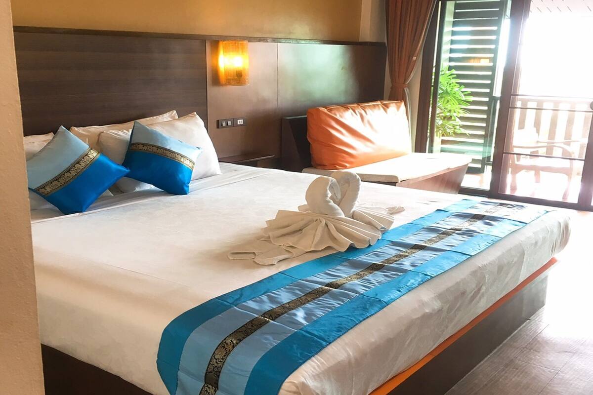 A hotel room with a large bed, a nightstand, a lamp, and a view of the outdoors.