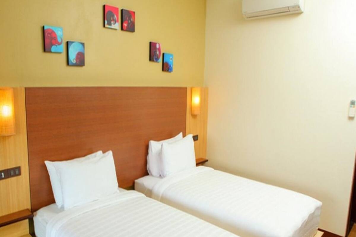 A hotel room with two single beds, wooden headboards, and a wall-mounted air conditioner.