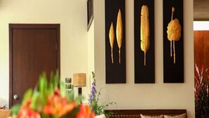 Una sala de estar con un sofá de madera, una puerta oscura y tres cuadros colgados en la pared que representan mazorcas de maíz.