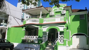 A green building with a balcony, a staircase, and a car parked in front. - Pousada Beira Mar (Santos)
