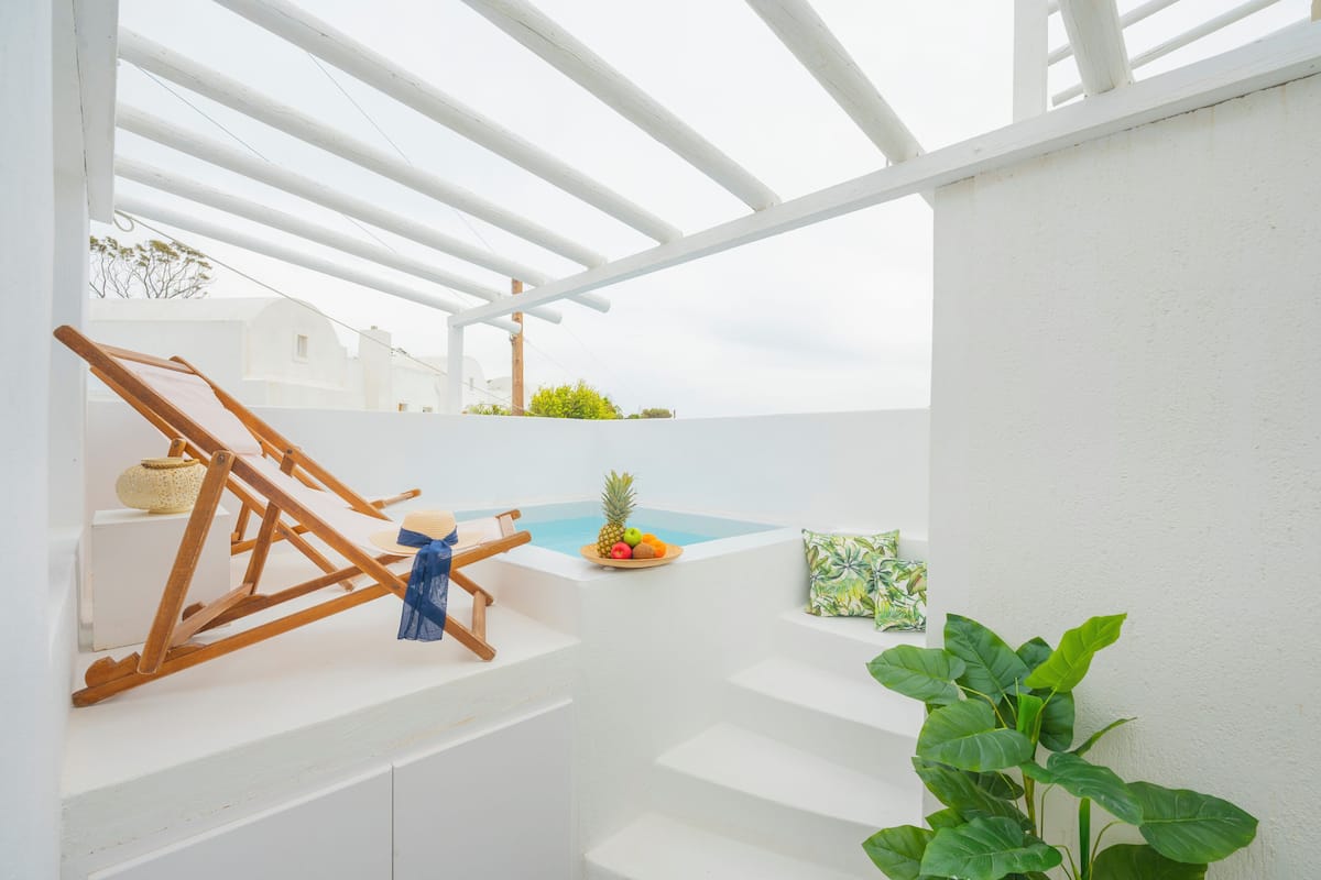 A white interior with a wooden chair, a small table with fruit, and a plant.