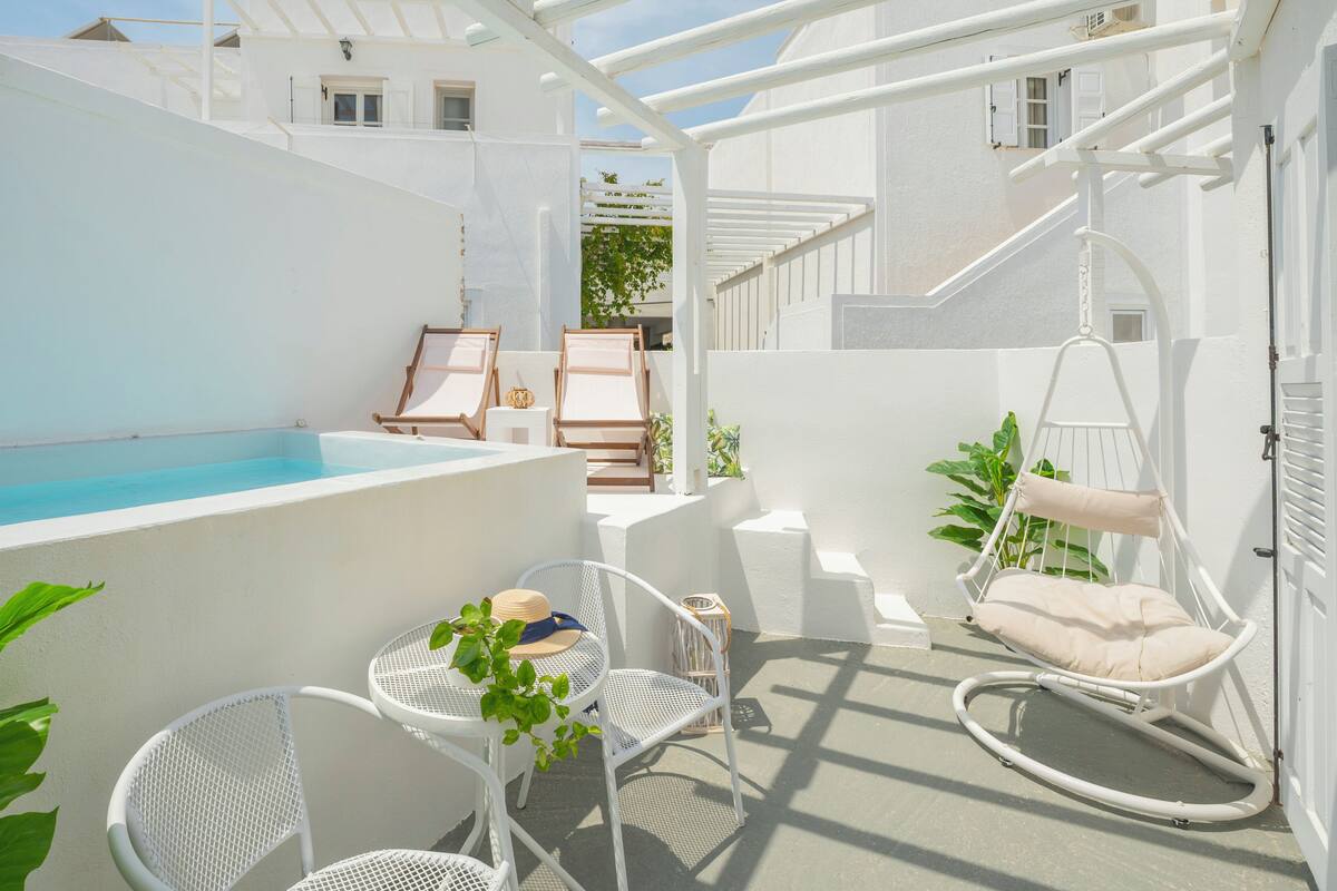 A rooftop terrace with a pool, white furniture, and hanging chairs.