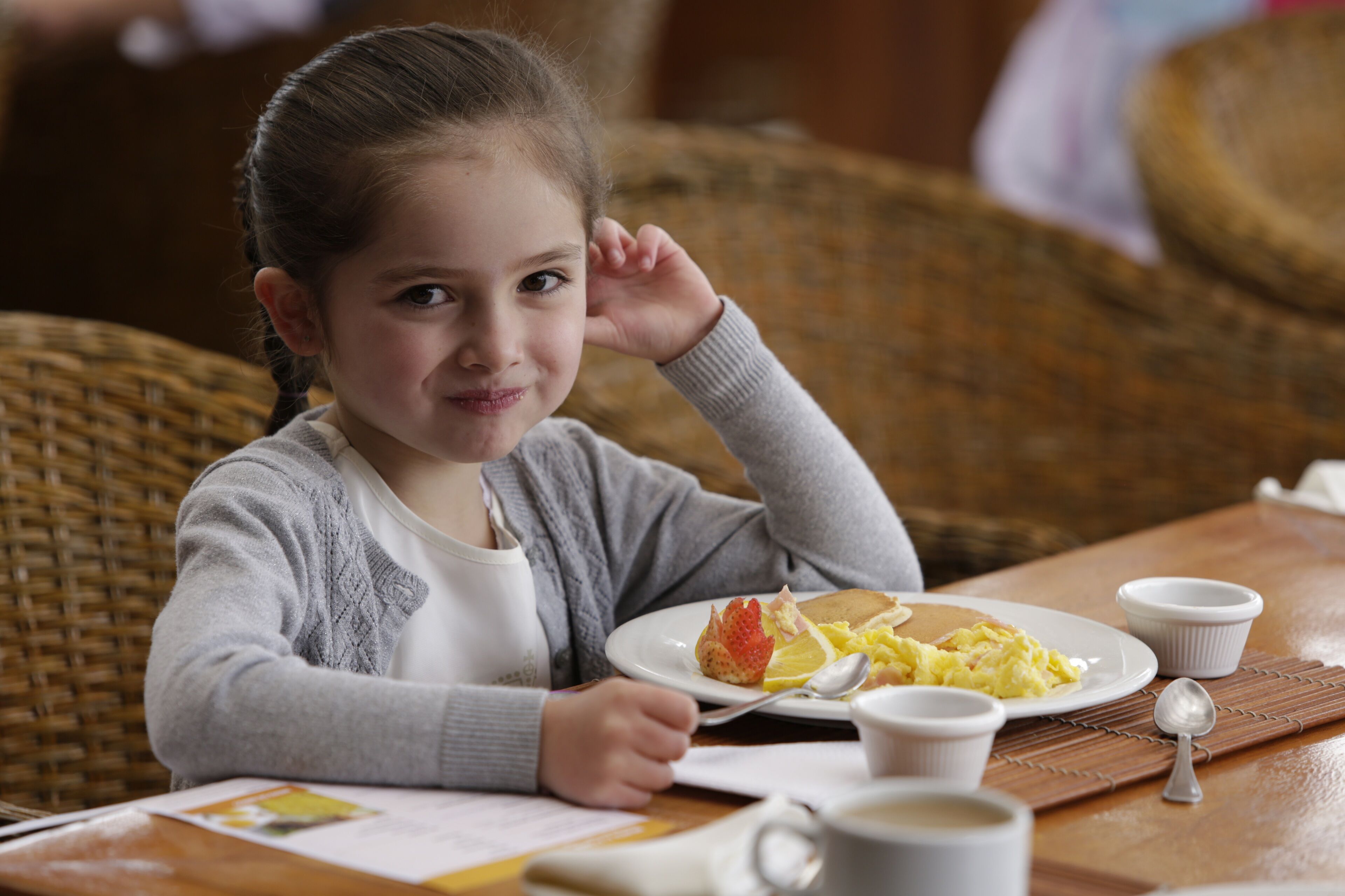 Un niño sentado a la mesa con alimentos para el desayuno, como huevos, tostadas y una taza de café.