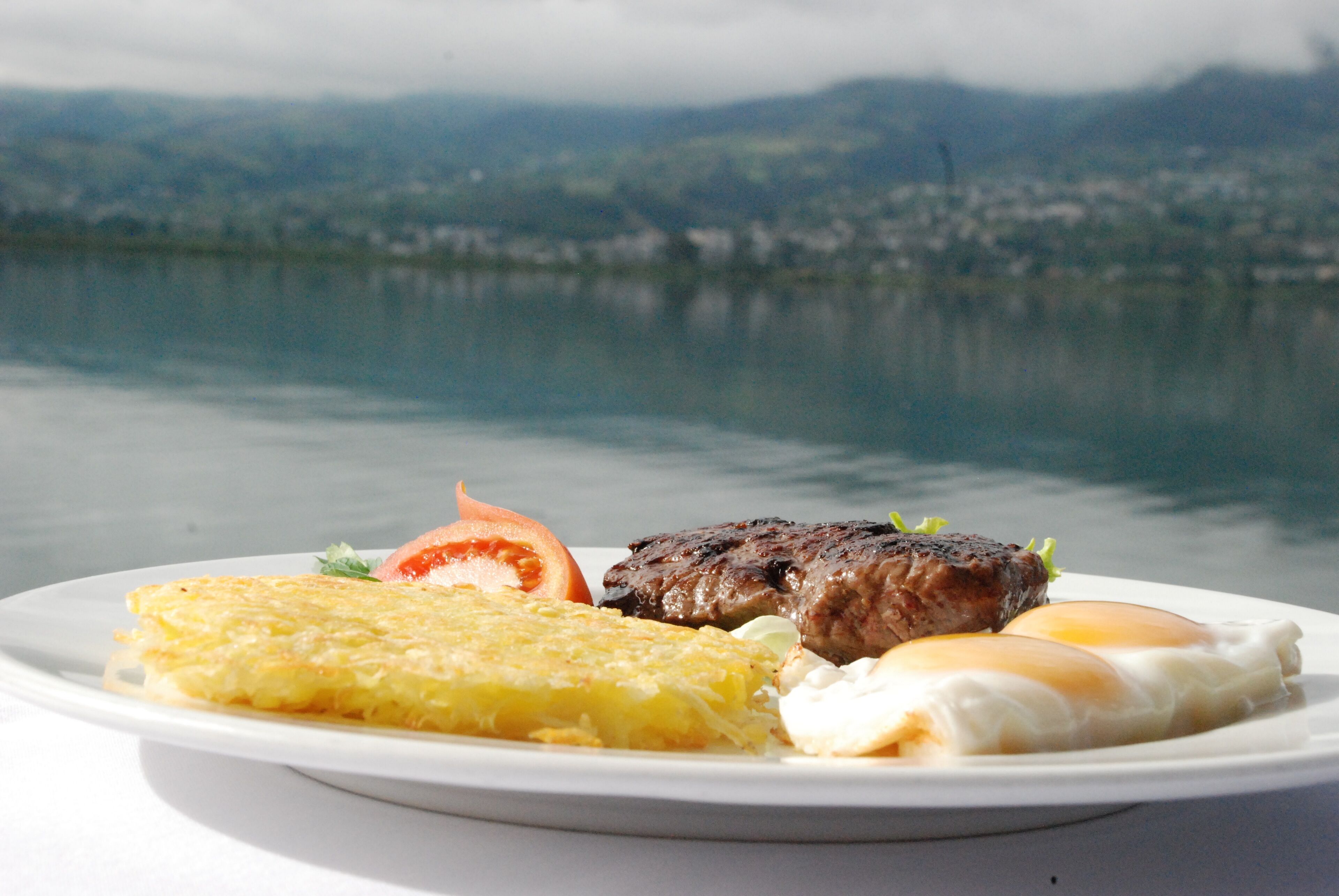 A plate of food with a view of a lake and mountains in the background.