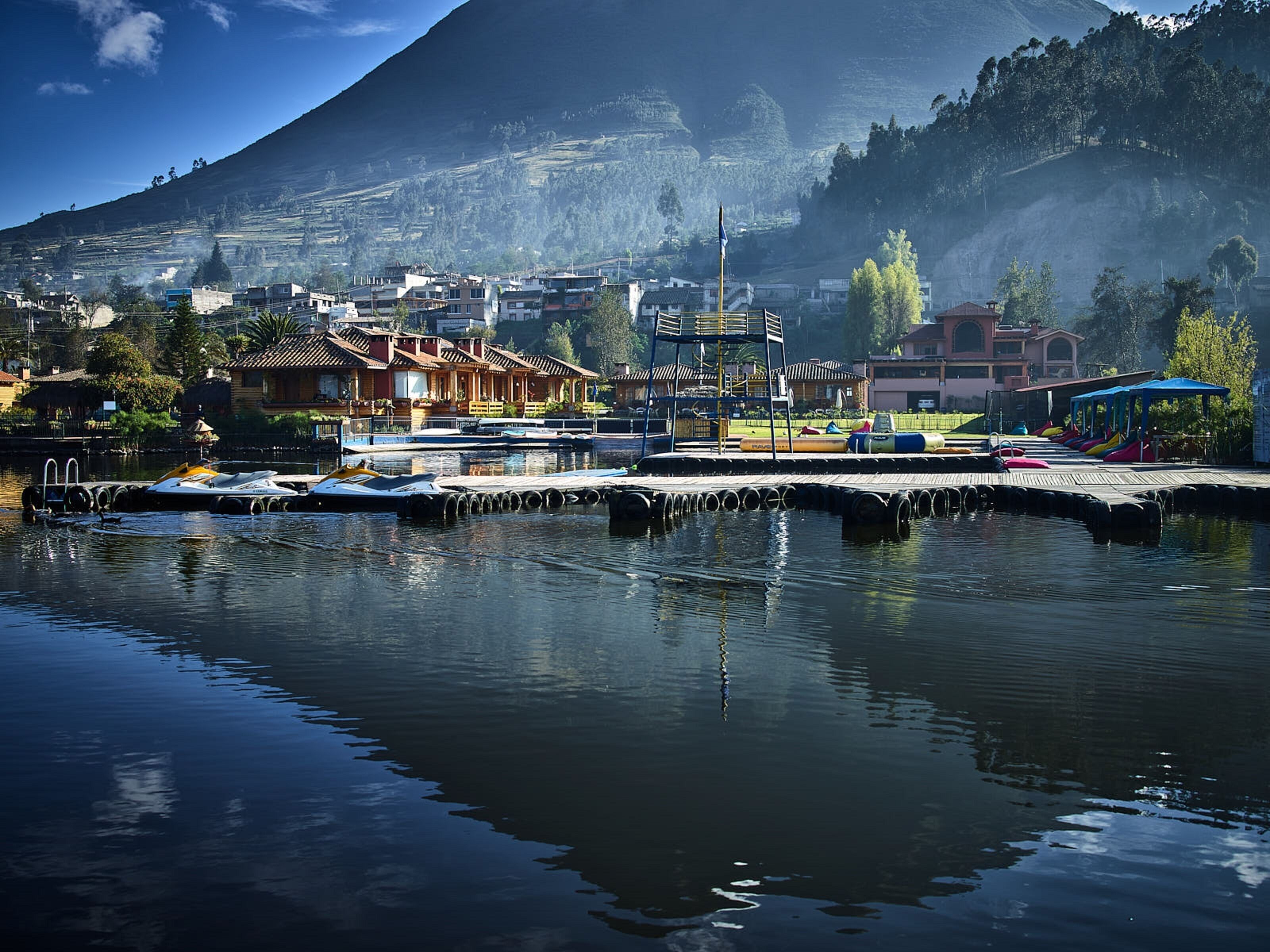 A waterfront area with buildings, a dock, and a mountain in the background.