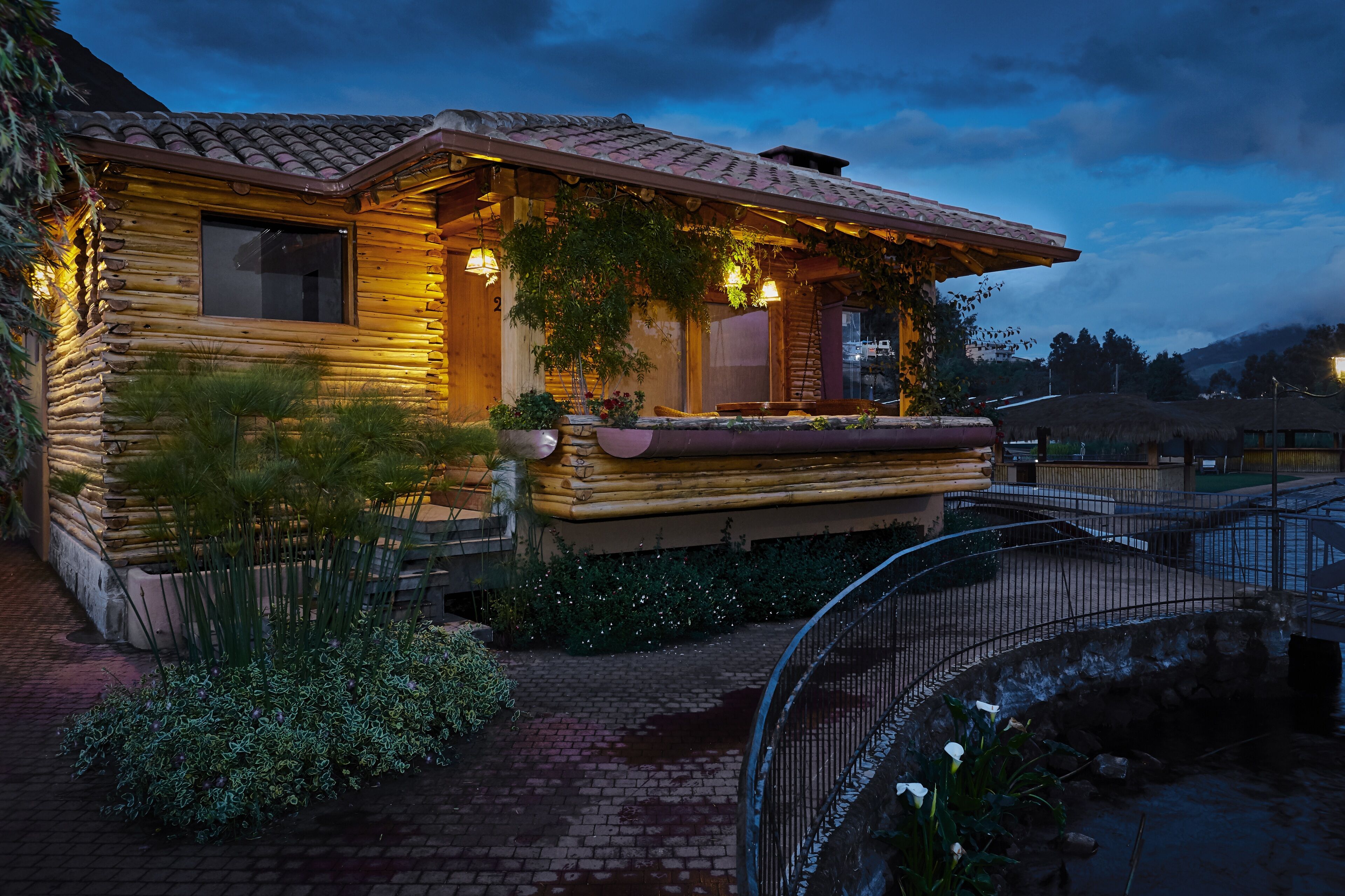 A log cabin with a thatched roof, a covered porch, and a small garden area with plants and a pathway.