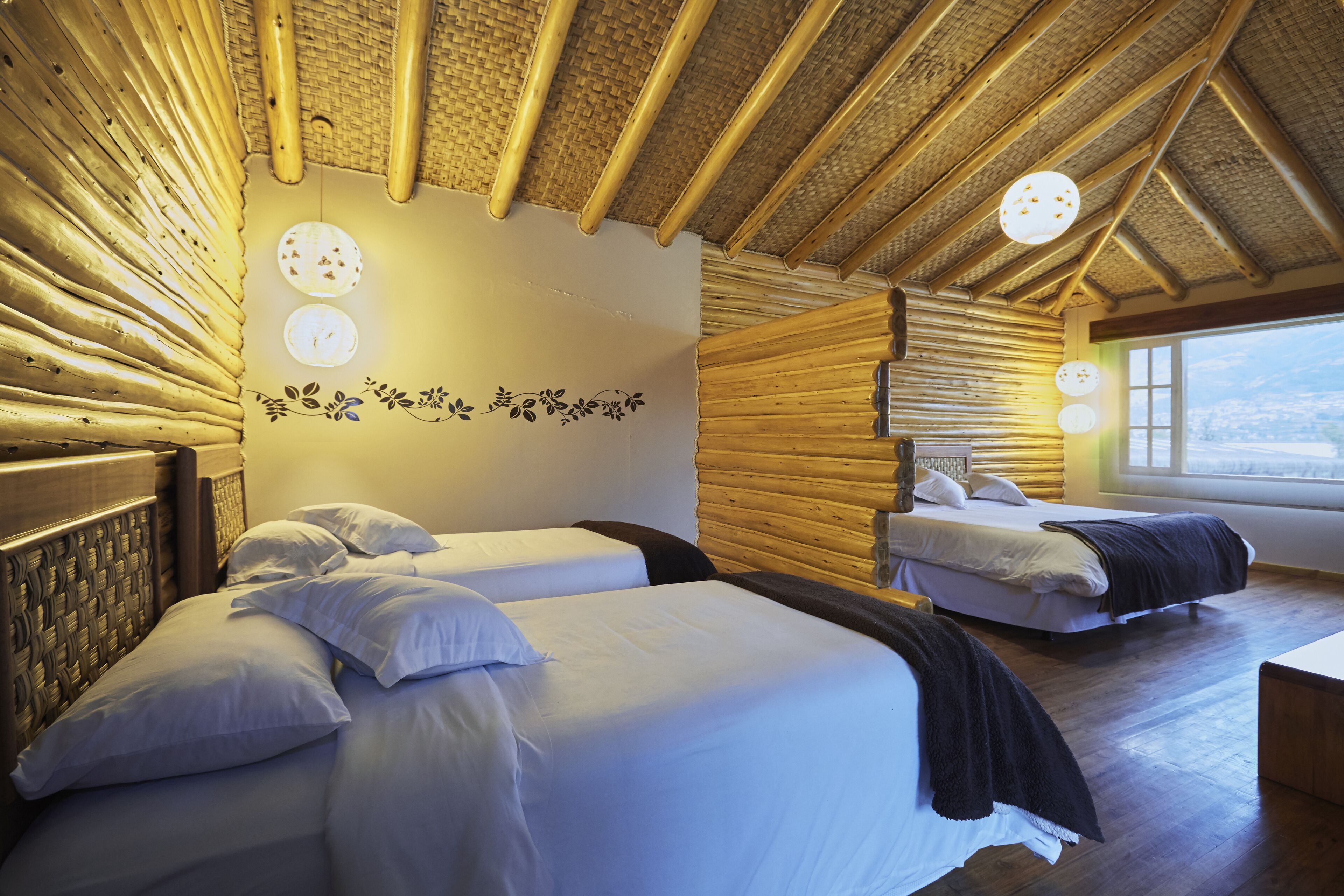 A room with two beds, a wooden ceiling, and a large window.