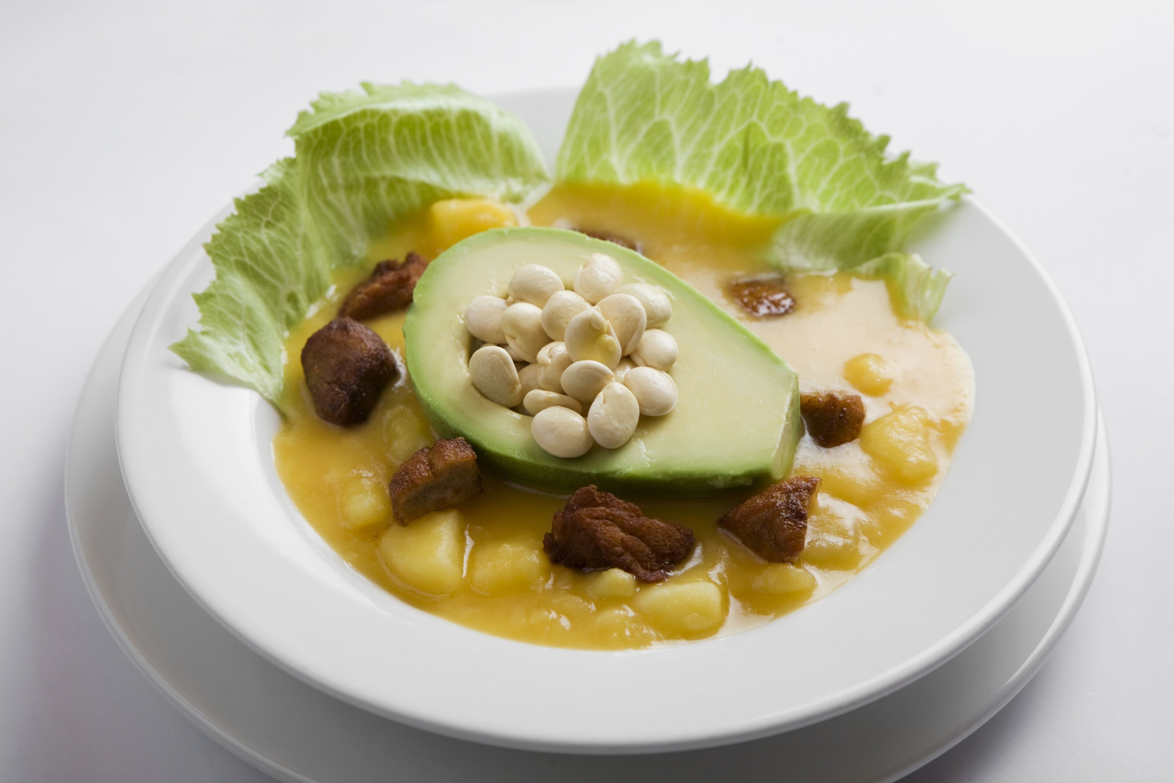 Un tazón de sopa con aguacate, frijoles y carne, adornado con lechuga.