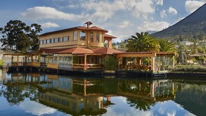 A large, multi-story house with a prominent tower, situated by a calm body of water, reflecting the structure. - Hostería Cabañas del Lago (San Pablo del Lago)