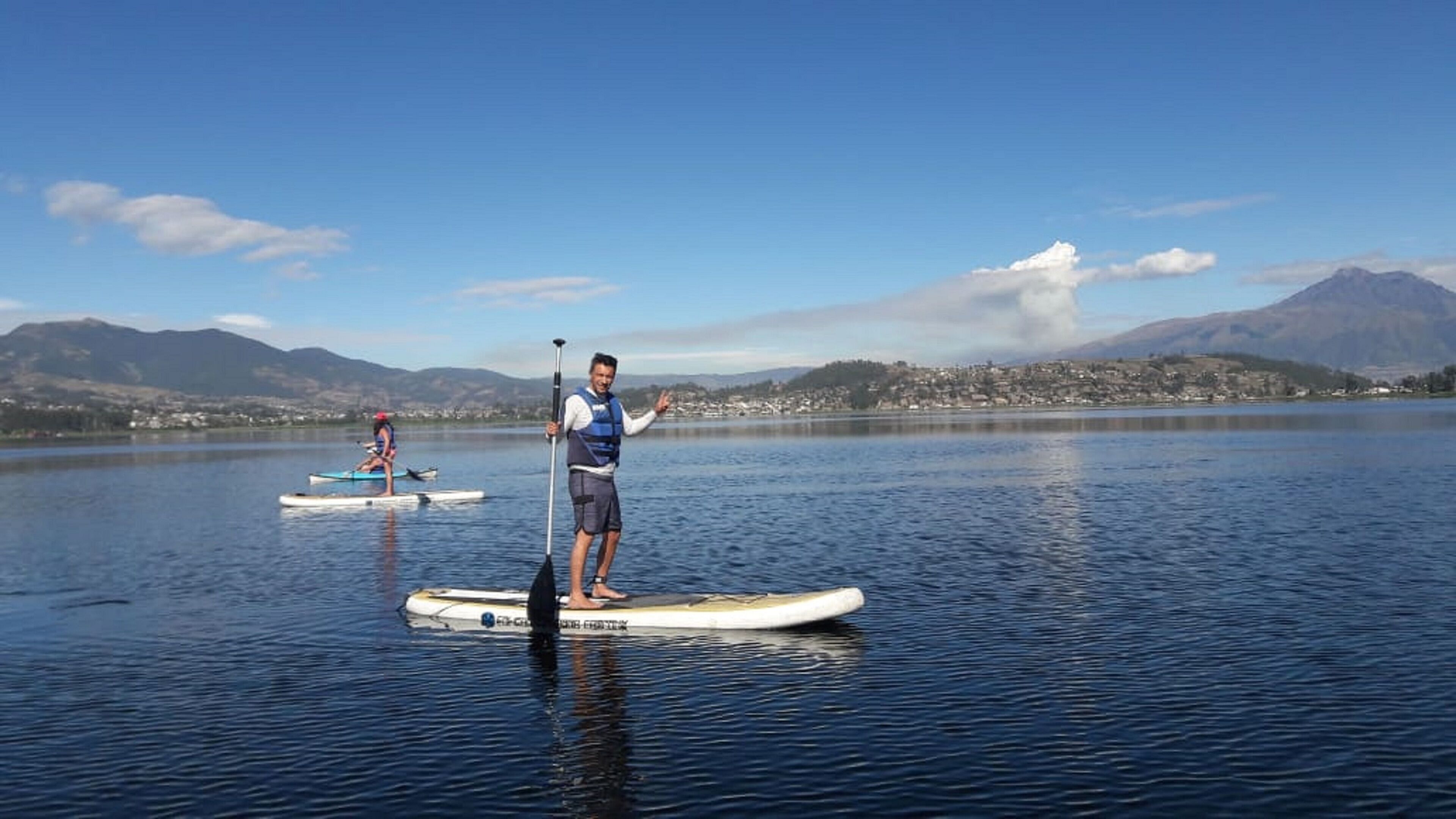 Dos personas haciendo paddleboard en un lago tranquilo con montañas al fondo.