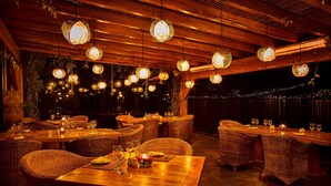 A restaurant with wooden tables and wicker chairs, hanging pendant lights, and a view of the night sky. - Hostería Cabañas del Lago (San Pablo del Lago)