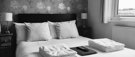 A neatly made bed with pillows and folded towels, a remote control, and a lamp on a bedside table.
