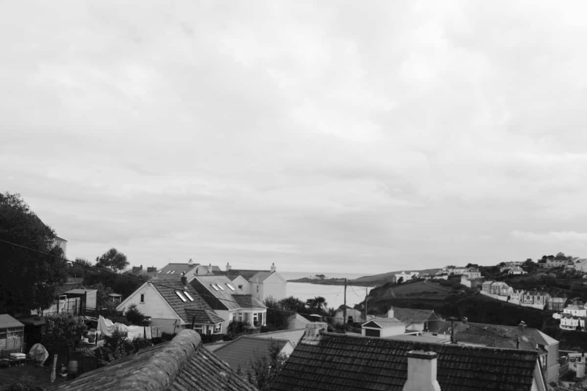 A black and white view of a coastal town with traditional houses, a prominent church, and a hill in the background.