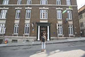Un edificio de ladrillo con entrada verde, varias ventanas y un cartel que indica zona de estacionamiento.