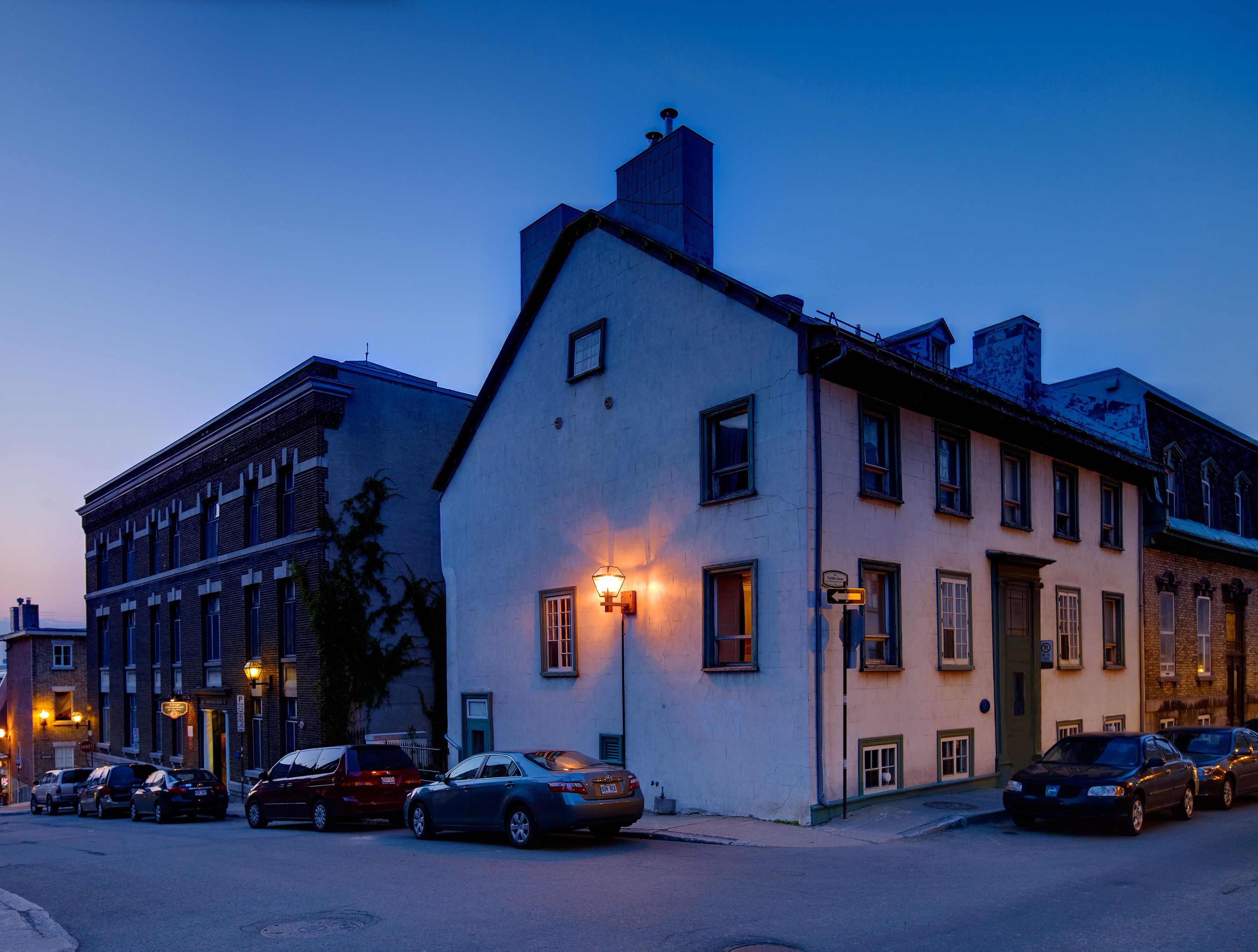 A street view at dusk with a row of parked cars and buildings.
