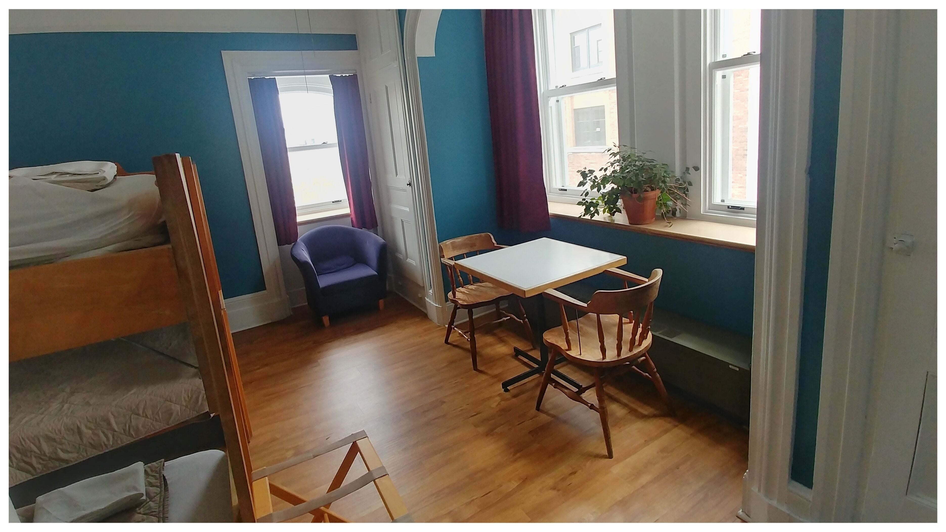 A room with bunk beds, a small table with chairs, a potted plant, and a window with curtains.