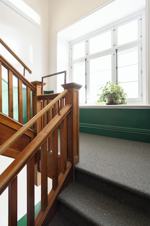 A wooden staircase with a handrail, carpeted steps, and a window with a potted plant. - Auberge Internationale de Québec - Hostel (Québec City)