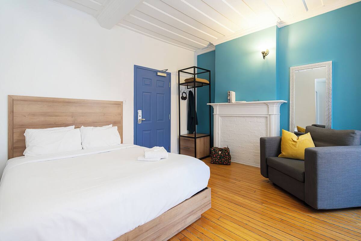 Un dormitorio con una cama, una puerta azul, una chimenea y un sofá gris.