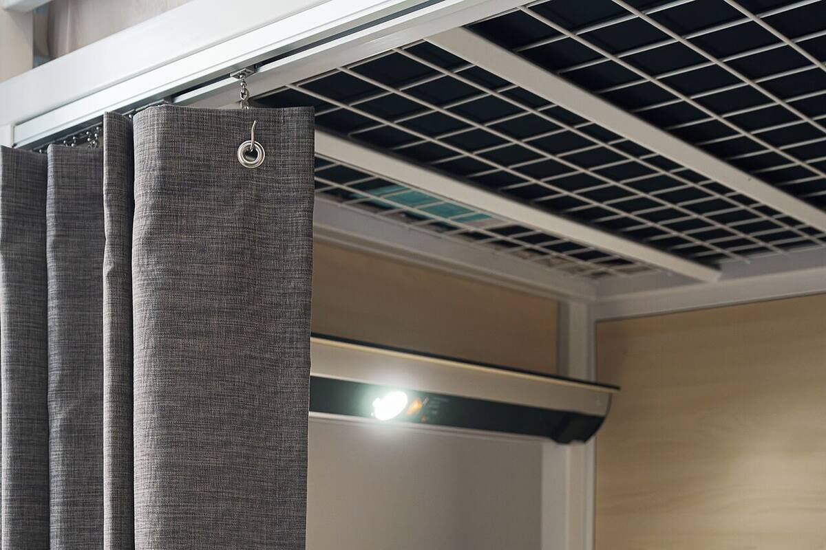 Una cama litera con cabecera, un almohadón blanco y cortinas grises.