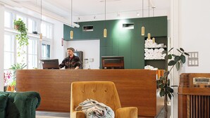 A reception area with a wooden reception desk, a green sofa, a yellow armchair, and a wooden coffee table with a potted plant. - Auberge Internationale de Québec - Hostel (Québec City)