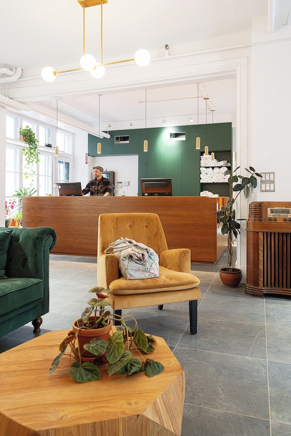 A reception area with a wooden reception desk, a green sofa, a yellow armchair, and a wooden coffee table with a potted plant. - Auberge Internationale de Québec - Hostel (Québec City)