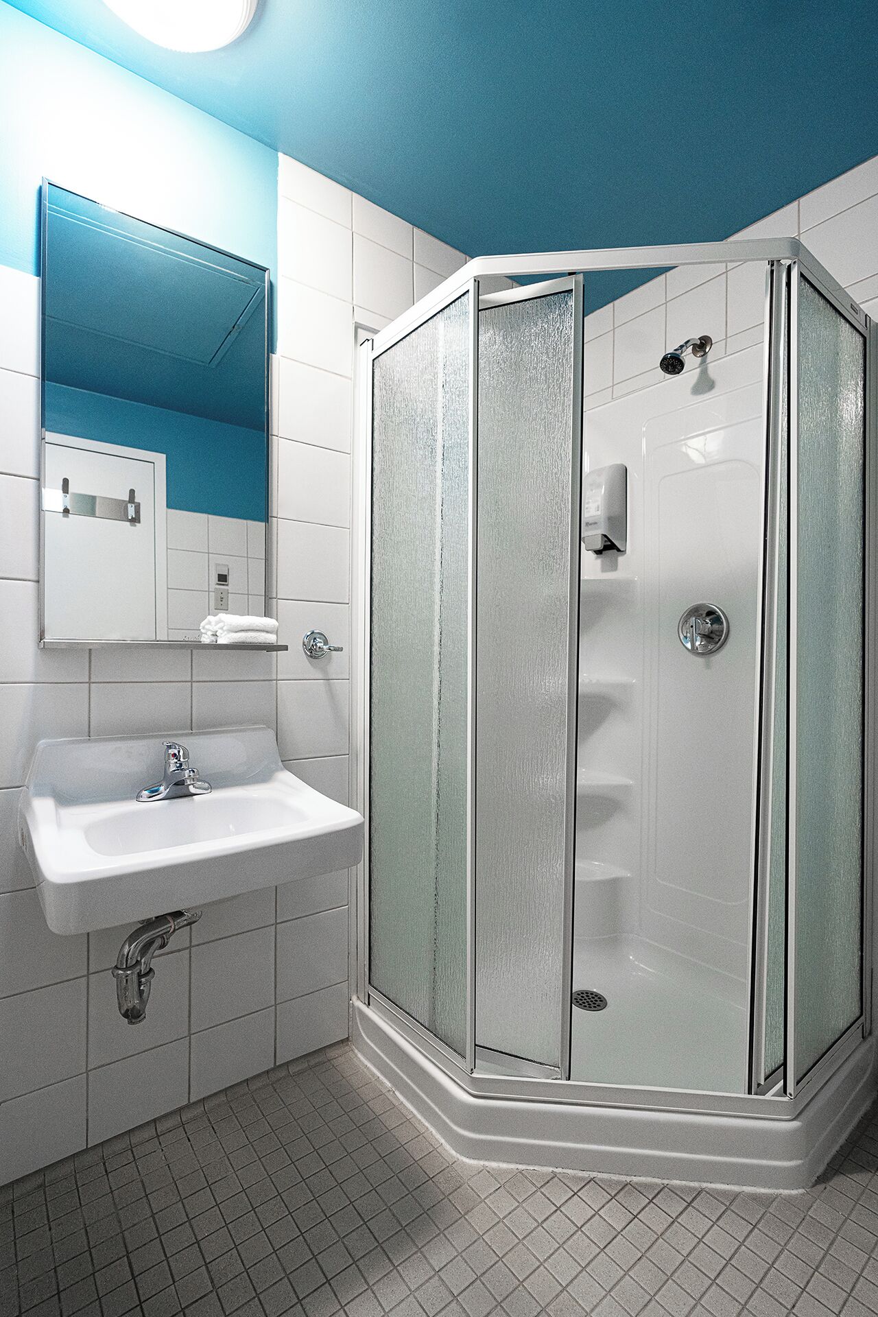 Un bany modern amb dutxa tancada per vidre, un lavabo blanc i un mirall sobre el lavabo.
