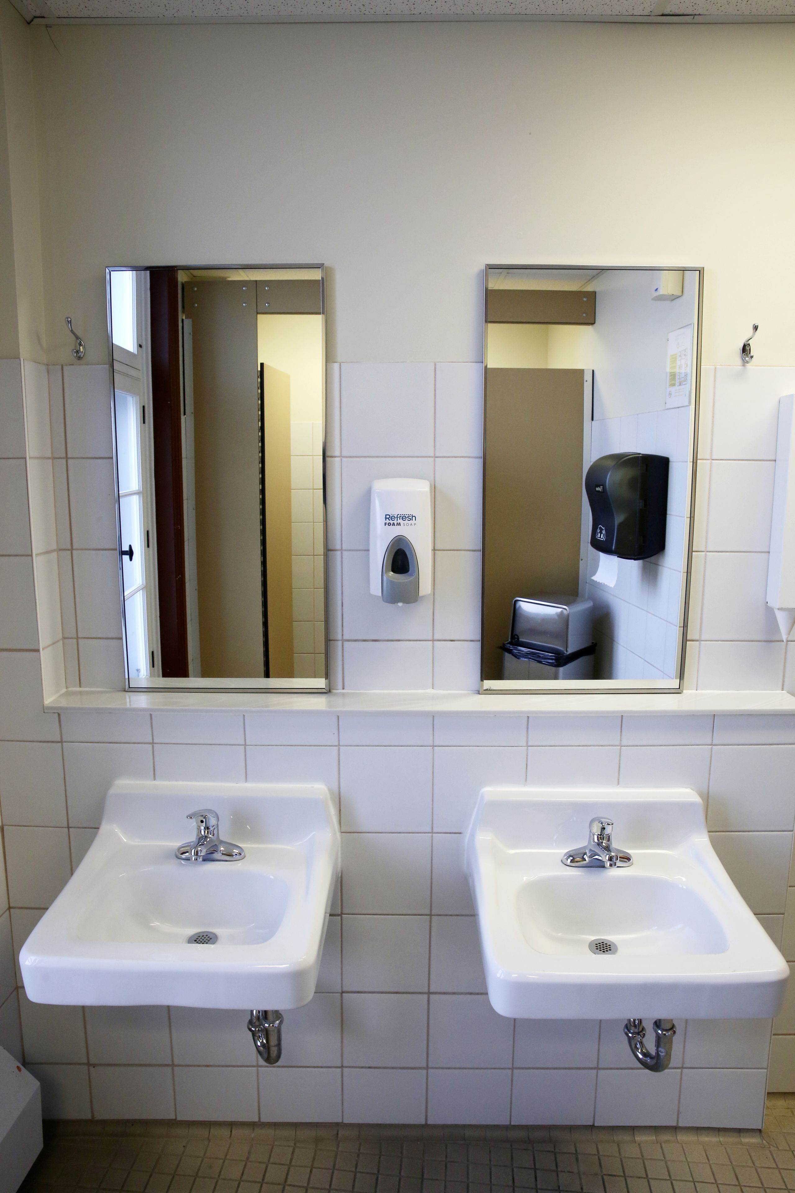 A restroom with two sinks, a mirror, a soap dispenser, and a paper towel dispenser.