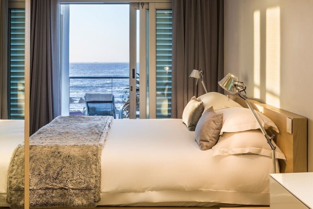 A hotel room with a bed, a bedside lamp, and a view of the ocean through large windows.